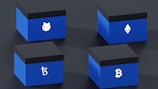 Four blue boxes are arranged in a 2x2 grid on a dark surface. Each box features a distinct cryptocurrency symbol in white: a dog face, Ethereum logo, Tezos logo, and Bitcoin logo.
