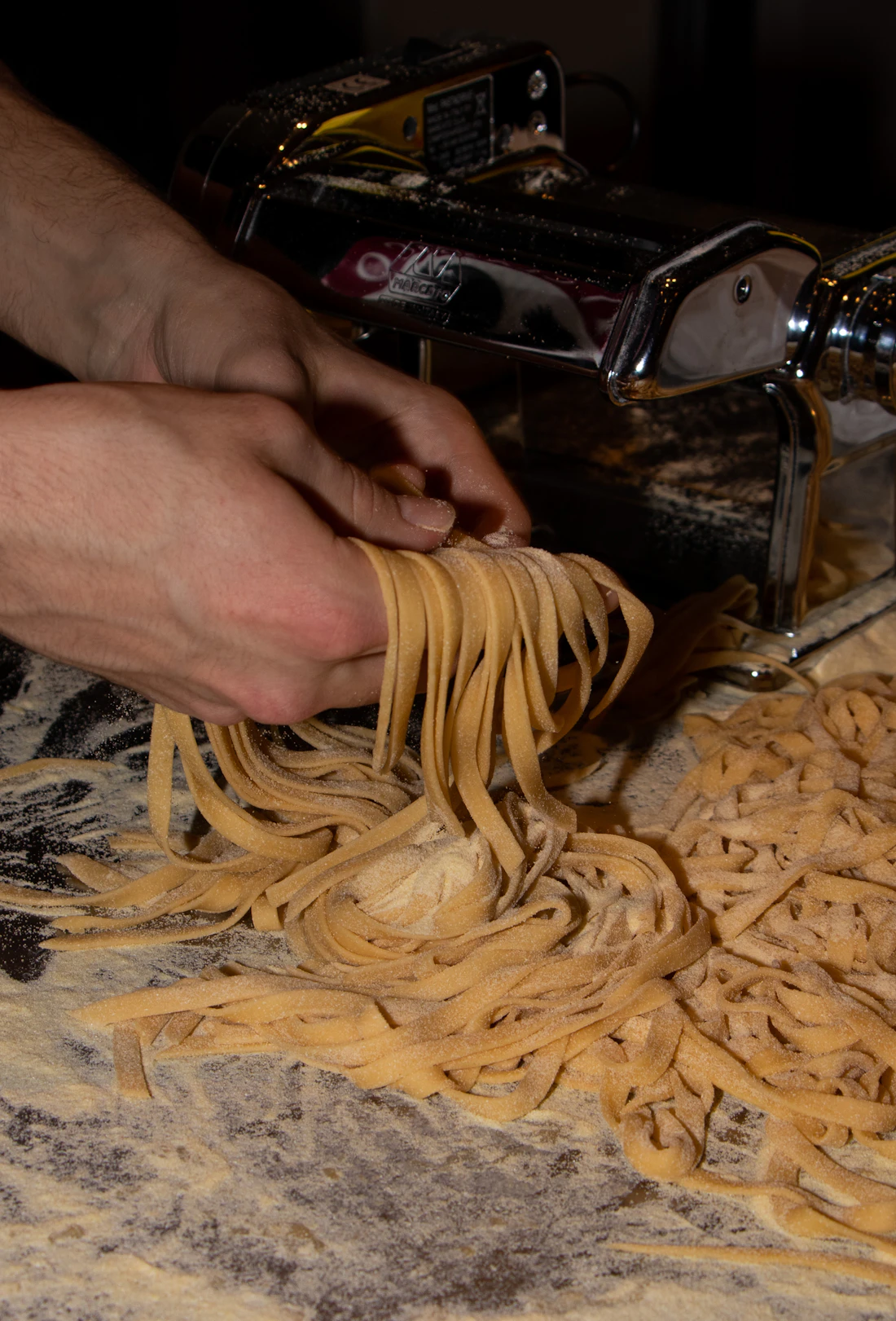 Floury hands lifting fresh-cut pasta ribbons on a flour-dusted table