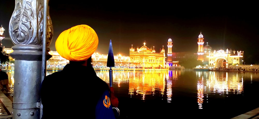 a man with a yellow turban standing next to a body of water