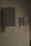A series of rectangular speakers are mounted on a wall in a row. The lighting is dim, casting faint shadows on the wall. The foreground shows one speaker in clear focus, while the others fade into the background.
