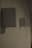 A series of rectangular speakers are mounted on a wall in a row. The lighting is dim, casting faint shadows on the wall. The foreground shows one speaker in clear focus, while the others fade into the background.