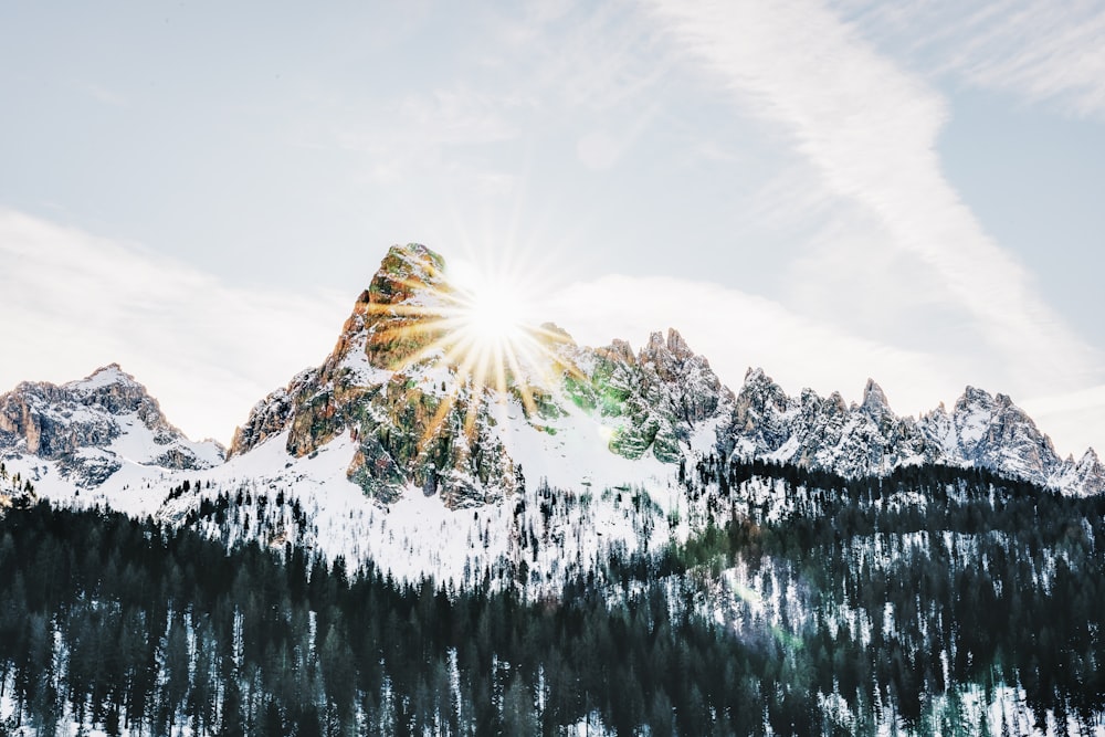 a mountain covered in snow with the sun shining through the clouds