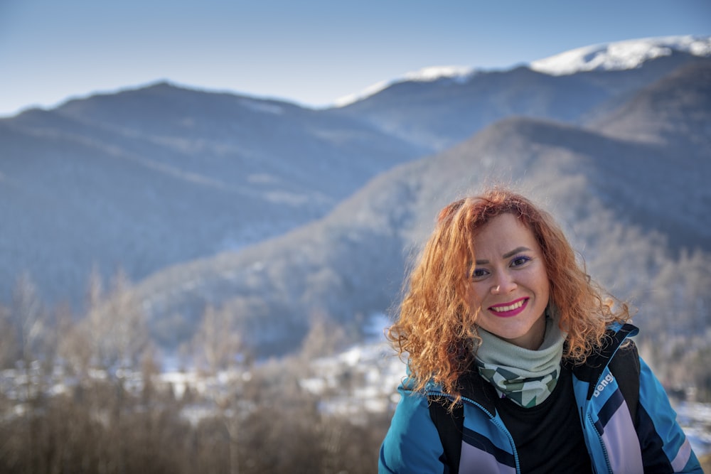 a woman with red hair standing in front of mountains