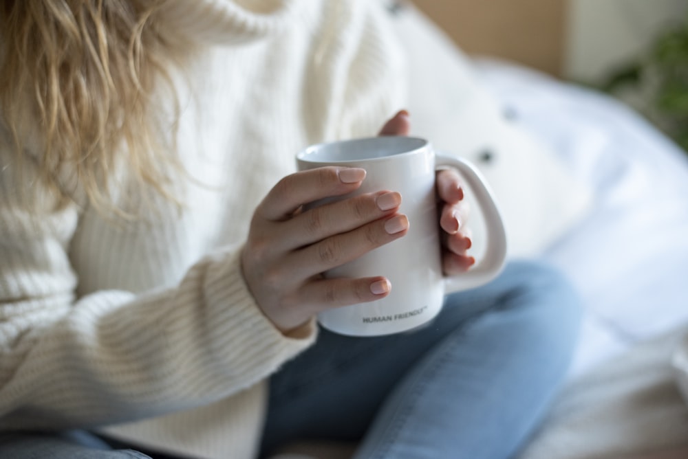 Eine Frau sitzt auf einem Bett und hält eine Kaffeetasse in der Hand
