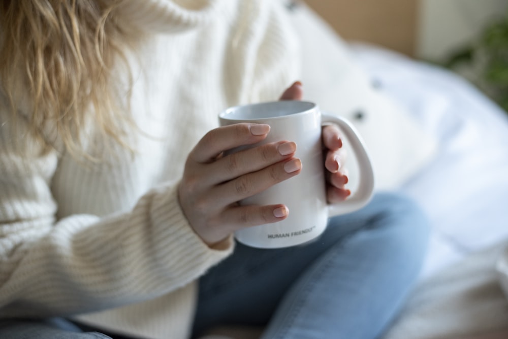 Una mujer sentada en una cama sosteniendo una taza de café