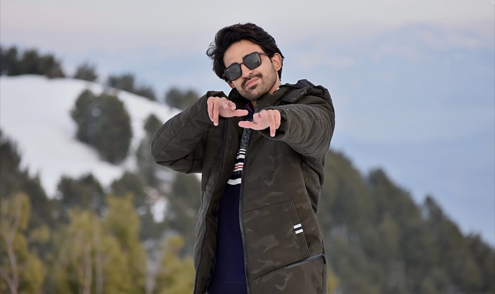 a man pointing at the camera with a mountain in the background