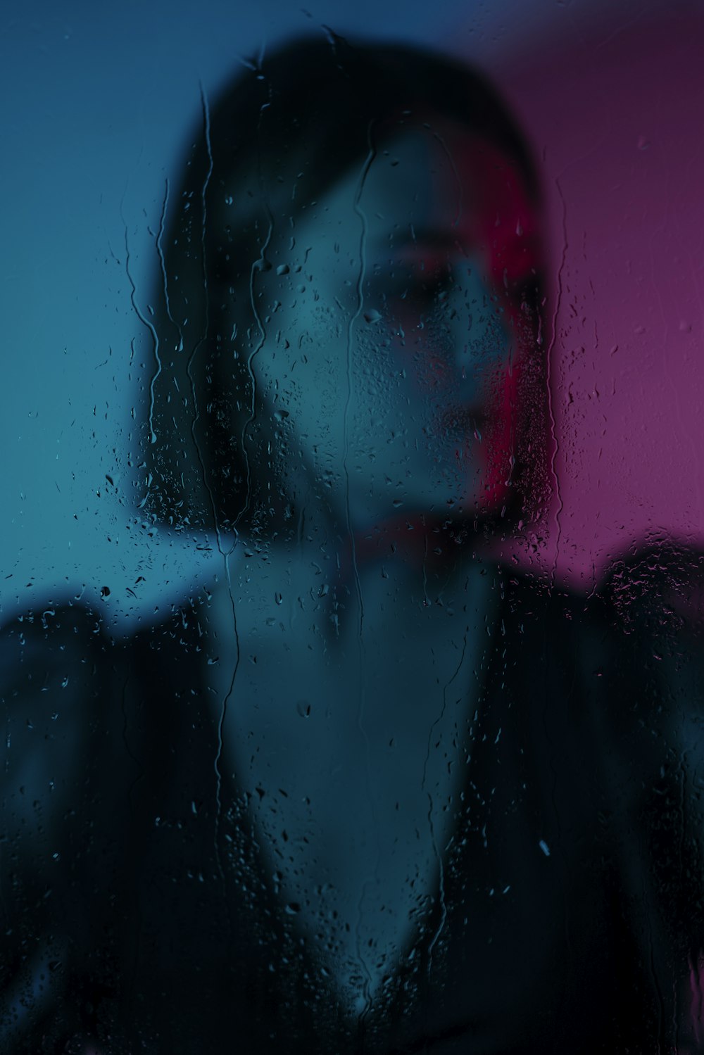 a woman standing in front of a window covered in rain