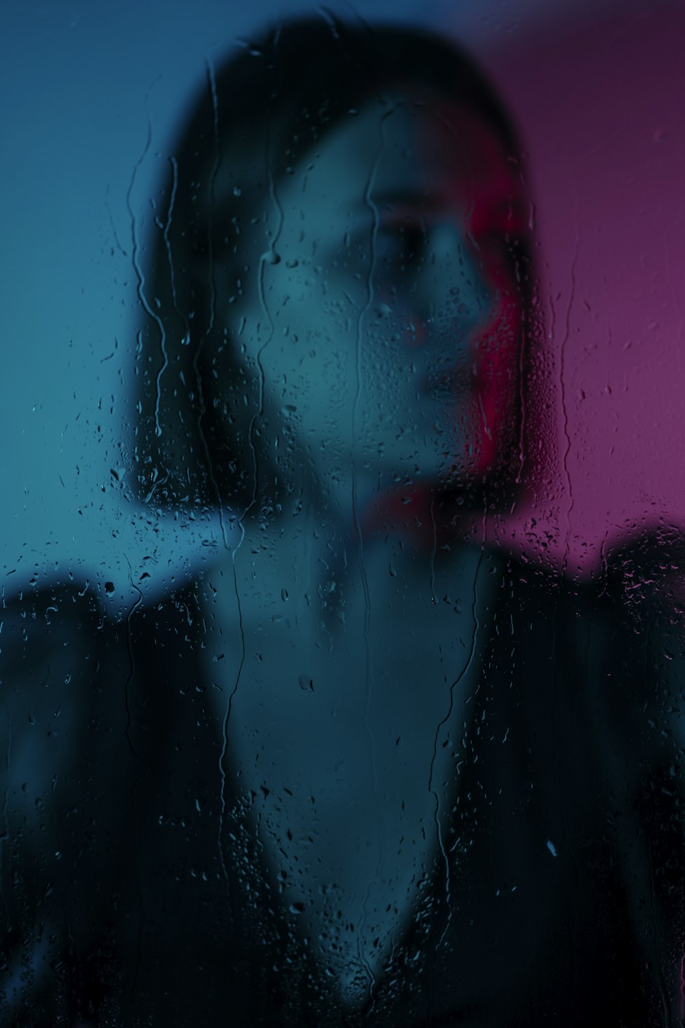 a woman standing in front of a window covered in rain