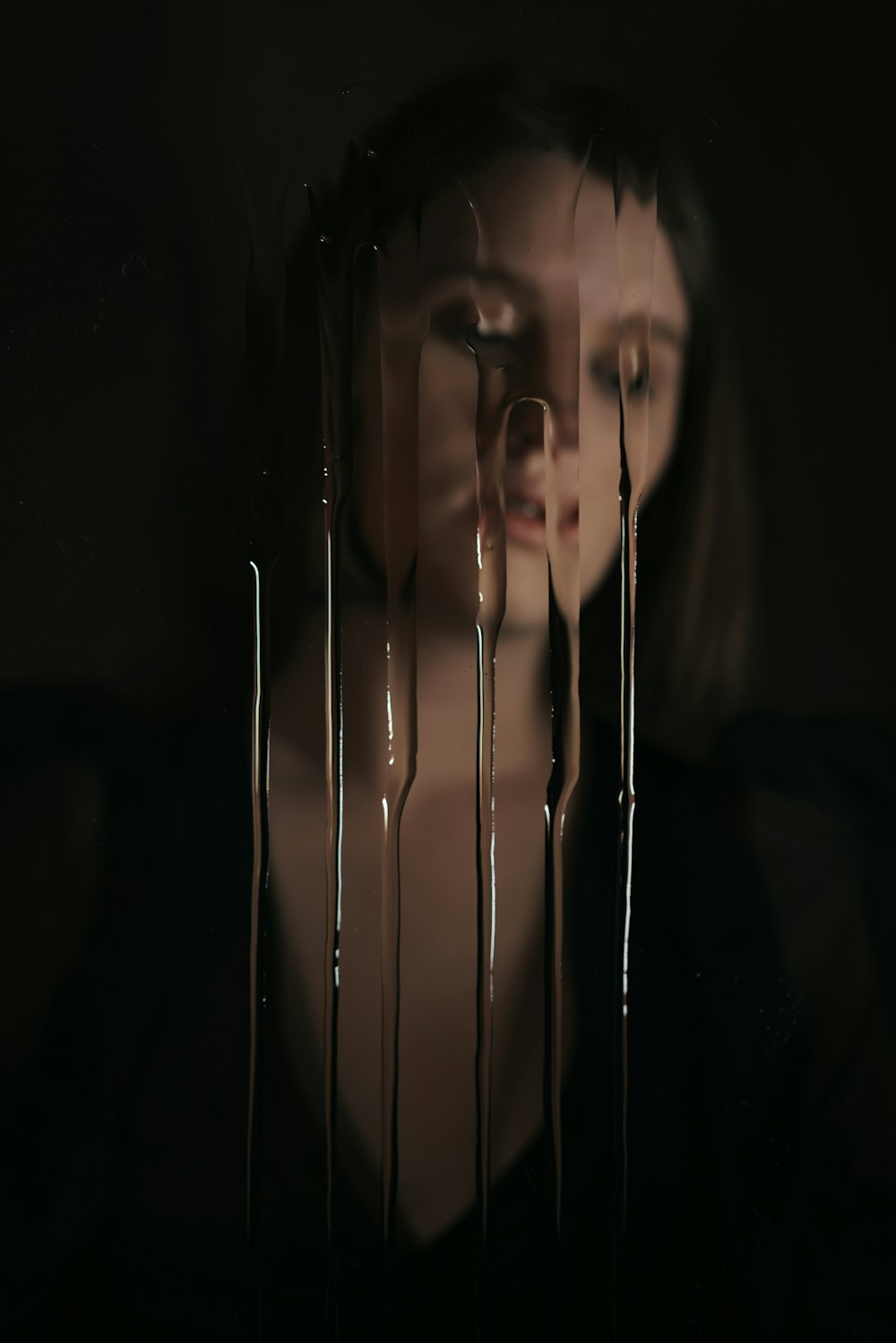 a woman standing in a dark room with dripping chocolate on her face