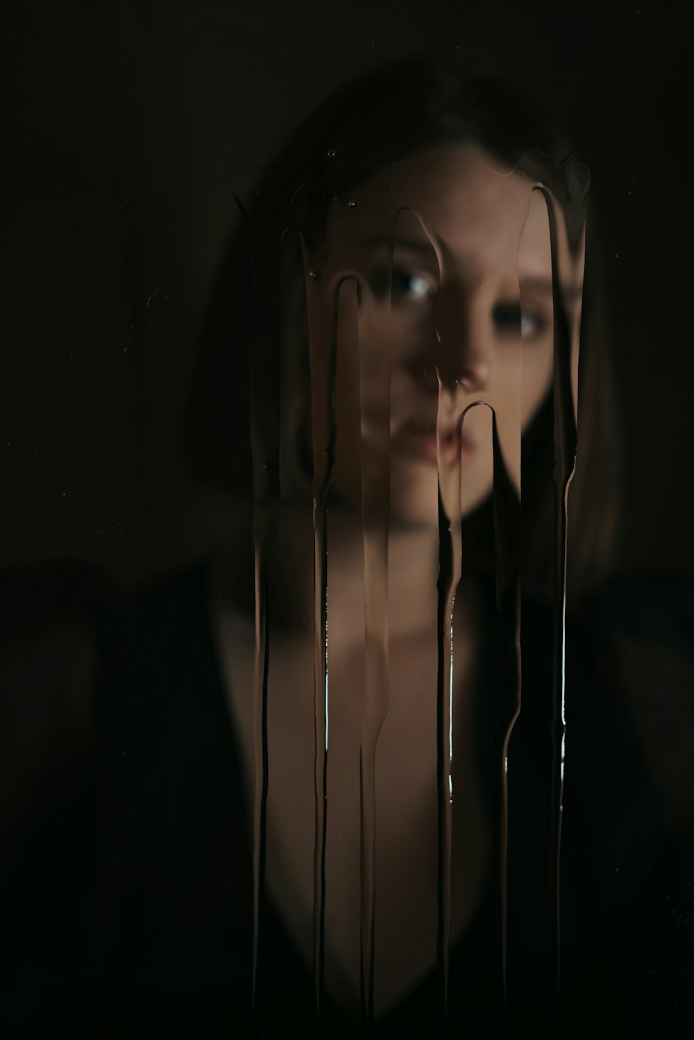 a woman standing in a dark room with dripping chocolate on her face