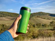 A travel mug nestled in a car cup holder with a scenic mountain road in the background.