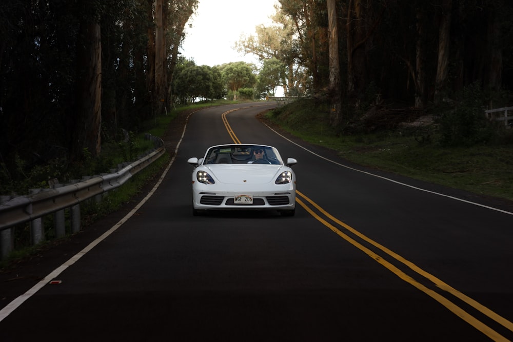 a white sports car driving down a tree lined road