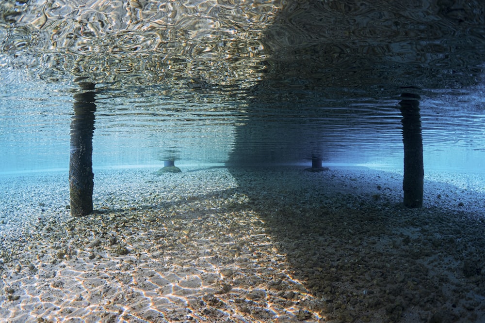 an underwater view of a sandy beach with two poles sticking out of the water