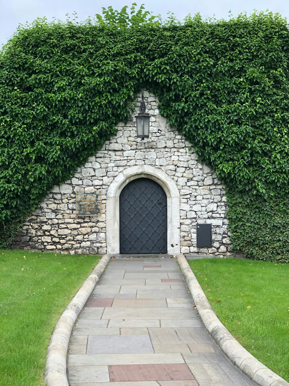 a stone building with a black door surrounded by greenery