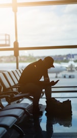 a man sitting at an airport looking at his cell phone