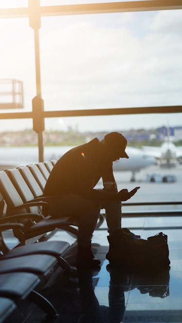 a man sitting at an airport looking at his cell phone