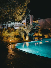 a large swimming pool surrounded by trees at night