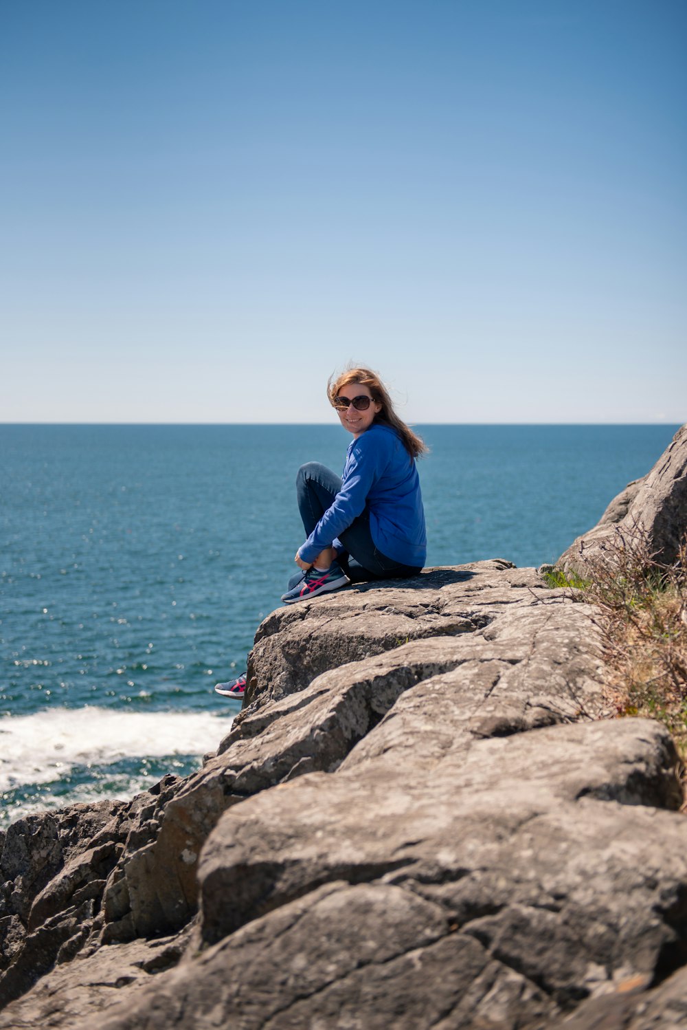 a woman sitting on top of a rock next to the ocean