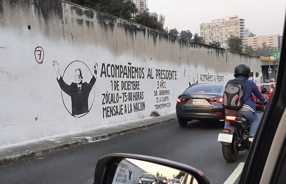 a man riding a motorcycle down a street next to a wall