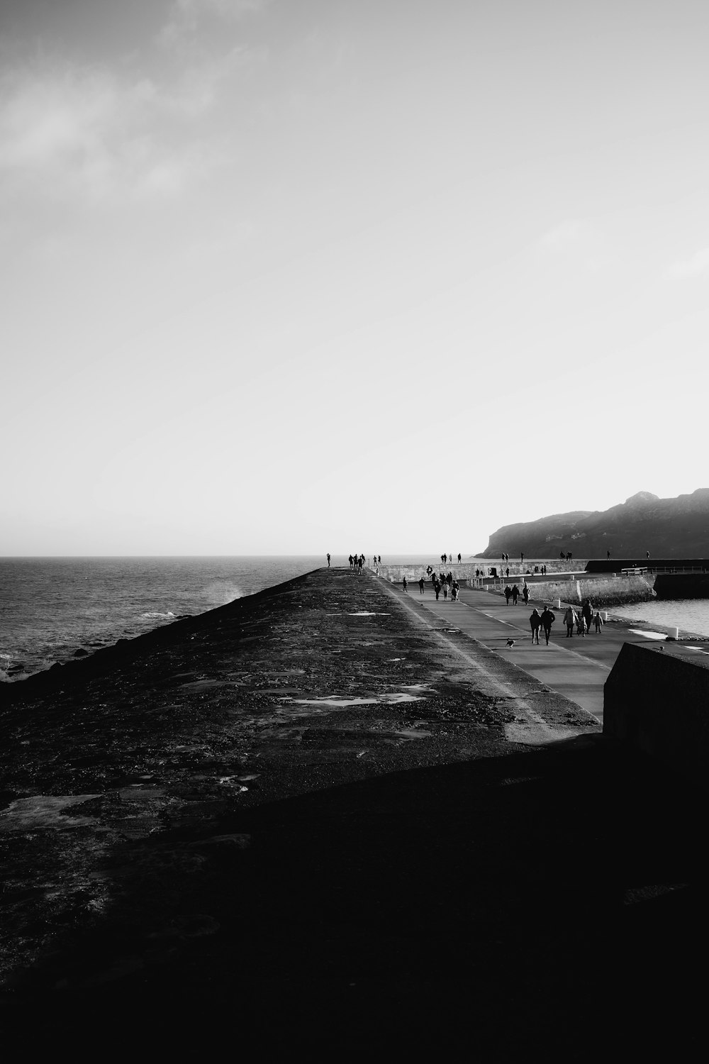 a black and white photo of people walking on a pier