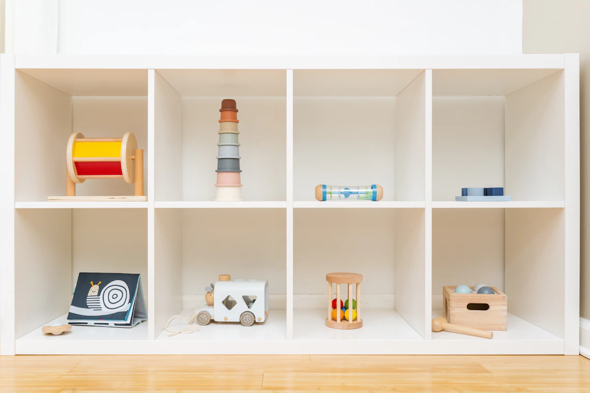 An open shelf holding a curated mix of wooden toys, soft toys and board books in a playroom