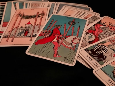 A collection of tarot cards is spread out, featuring various illustrated scenes and symbols. Dominant cards include a figure on horseback holding a staff, and another card shows a structure with four tall poles surrounding it.