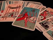 A collection of tarot cards is spread out, featuring various illustrated scenes and symbols. Dominant cards include a figure on horseback holding a staff, and another card shows a structure with four tall poles surrounding it.