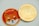 A close-up view of two coins placed side by side. The left coin features a cartoon Shiba Inu dog in orange with the word '$SHIB' on a red background. The right coin appears to have intricate engravings with the design resembling a digital currency, featuring the words 'QUANTITATIVE' and 'CRYPTOCURRENCY TOKEN'. Both coins have a reflective, gold-colored border.