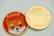 A close-up view of two coins placed side by side. The left coin features a cartoon Shiba Inu dog in orange with the word '$SHIB' on a red background. The right coin appears to have intricate engravings with the design resembling a digital currency, featuring the words 'QUANTITATIVE' and 'CRYPTOCURRENCY TOKEN'. Both coins have a reflective, gold-colored border.
