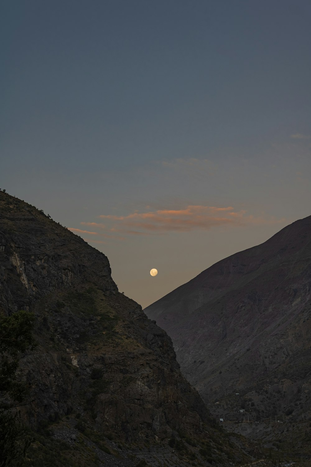 the moon is setting over a mountain range