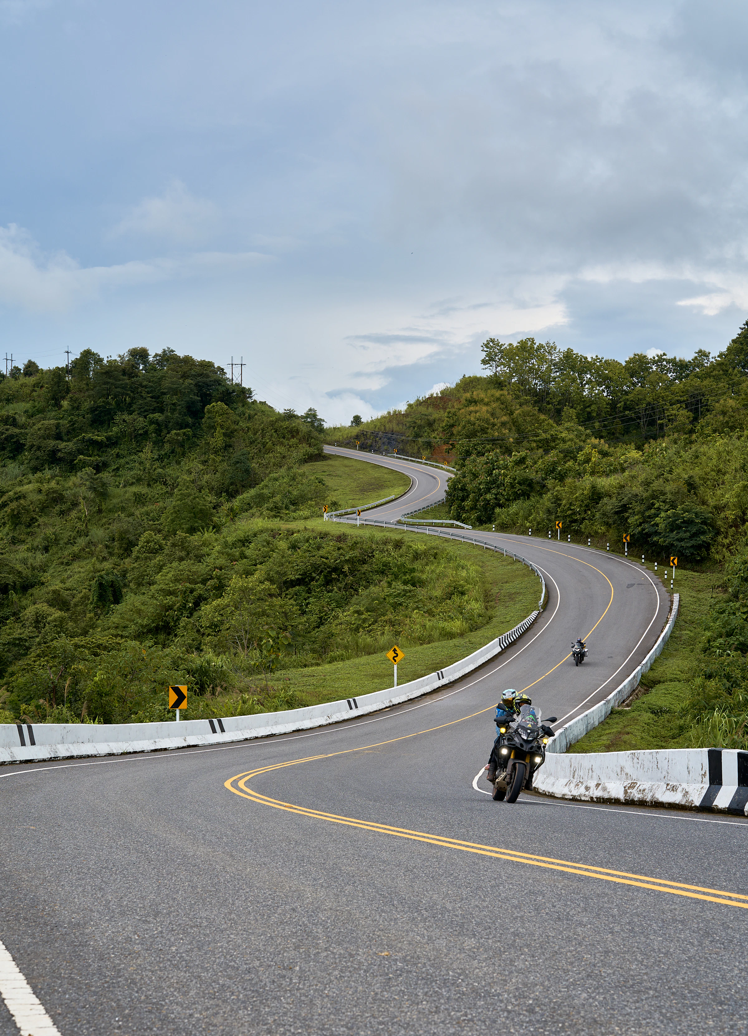 Motard penché en virage sur une route de montagne sinueuse — illustration surestimation et chute solo