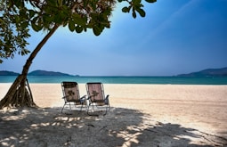 a couple of chairs sitting on top of a sandy beach