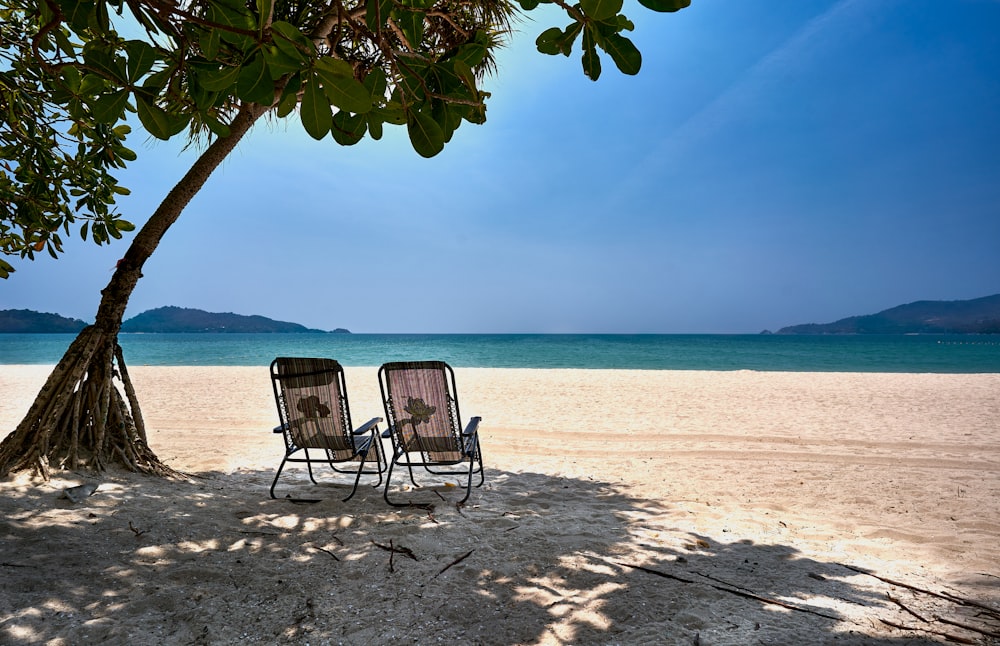 a couple of chairs sitting on top of a sandy beach