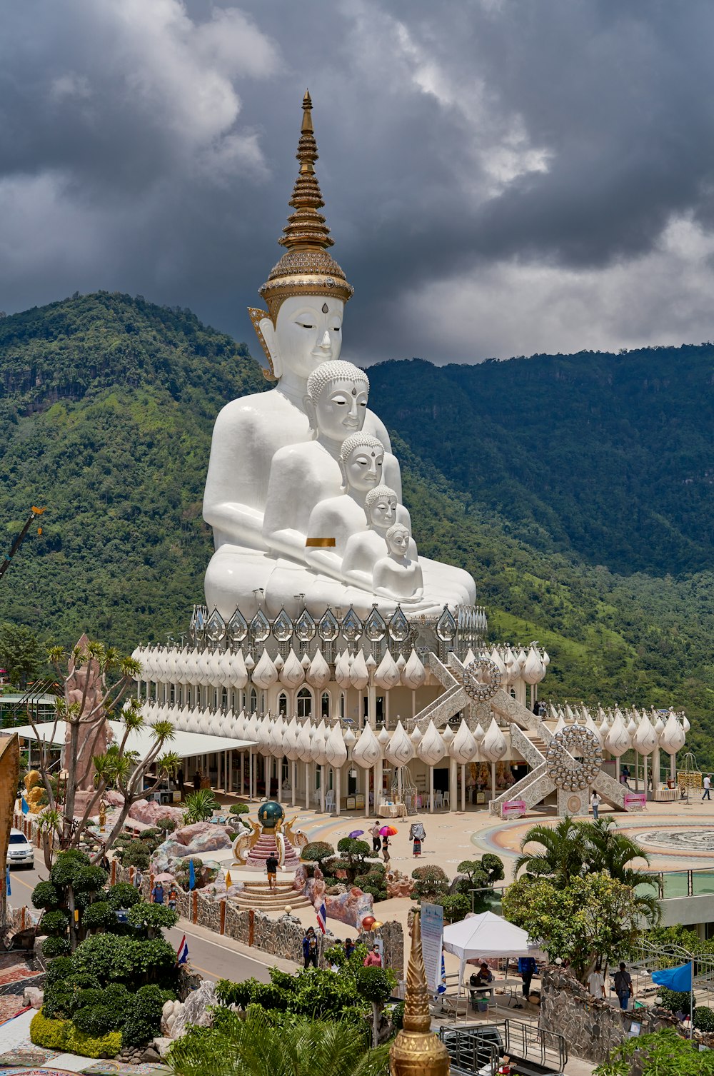 a large white buddha statue sitting on top of a lush green hillside