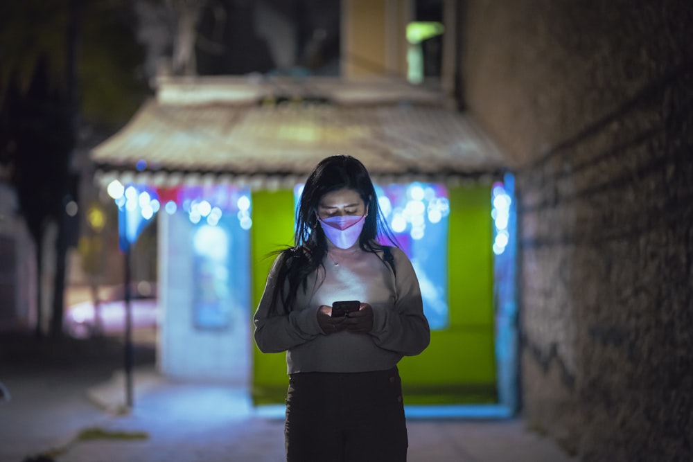 a woman standing on a street at night using a cell phone