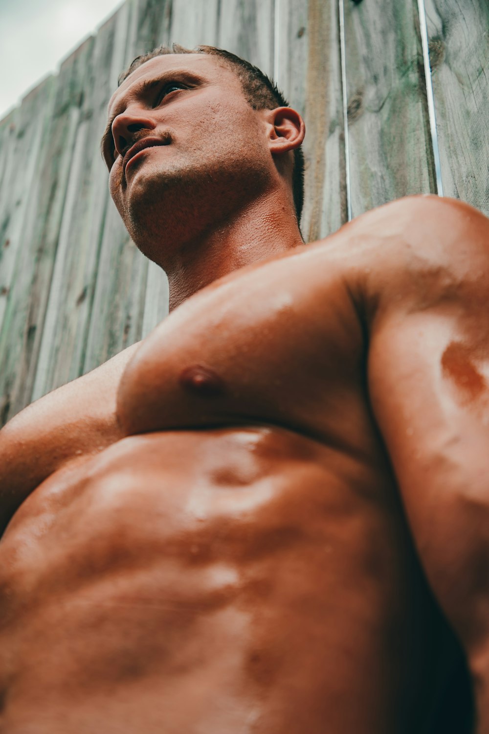 a man without a shirt standing in front of a wooden wall