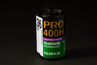 A roll of Fujifilm Pro 400H color negative film is displayed prominently. The cylindrical film canister is upright with a label indicating it is a professional-grade film with 36 exposures. The label features white, purple, and green colors, with bold yellow lettering for the film type and the Fujifilm logo.