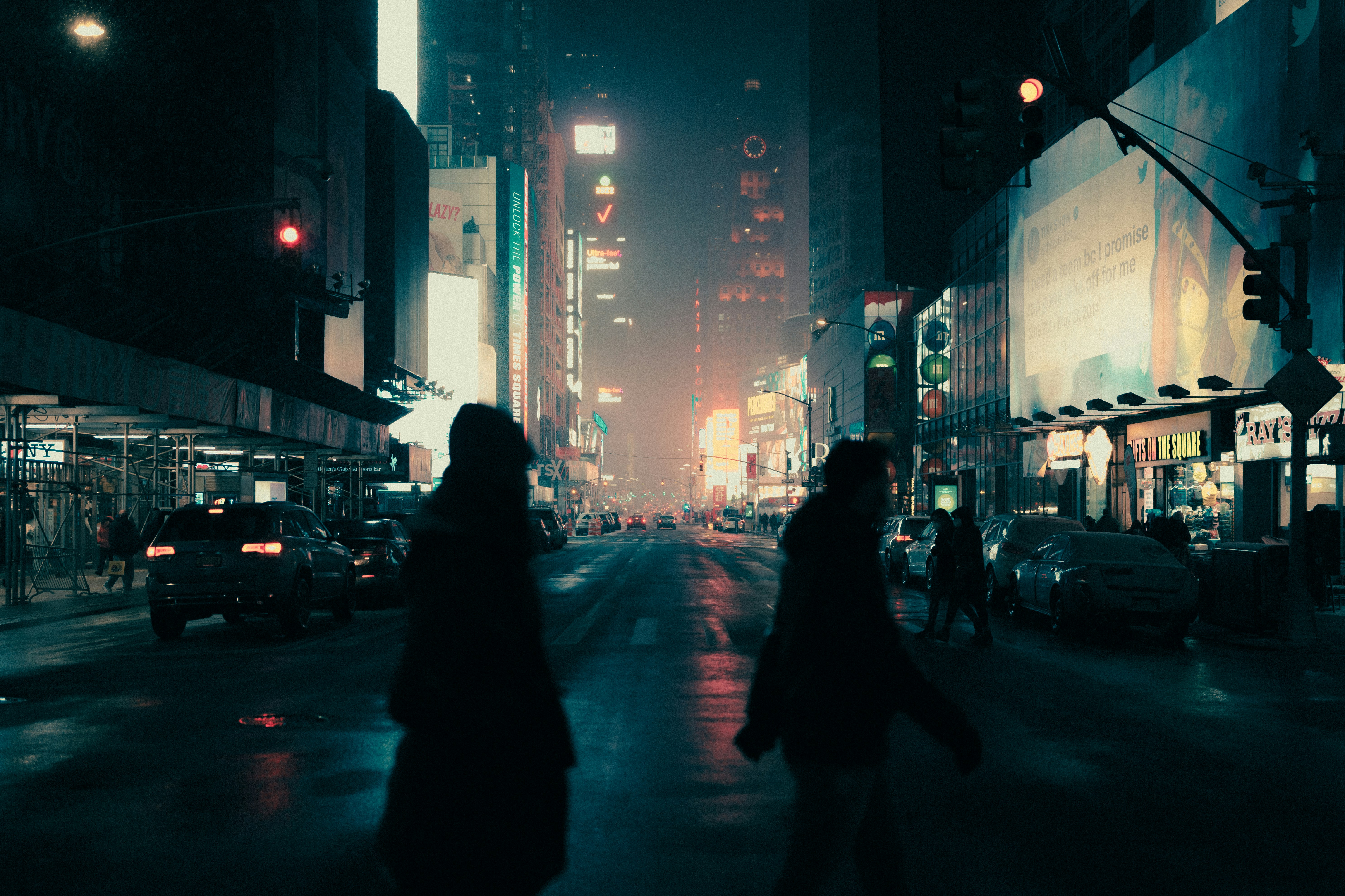 a couple of people walking across a street at night