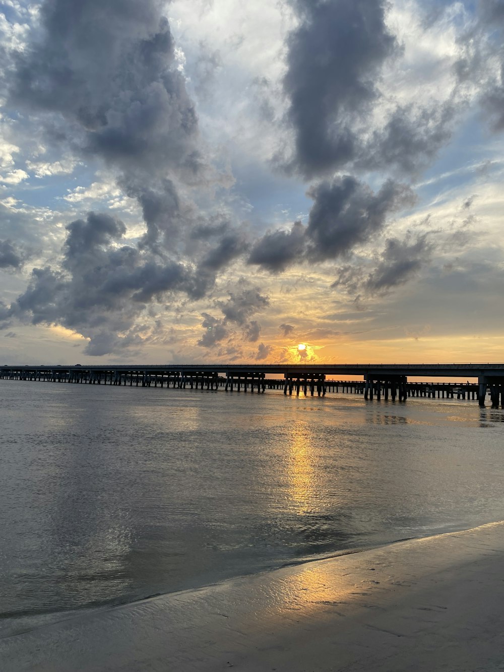 the sun is setting over the ocean with a pier in the distance