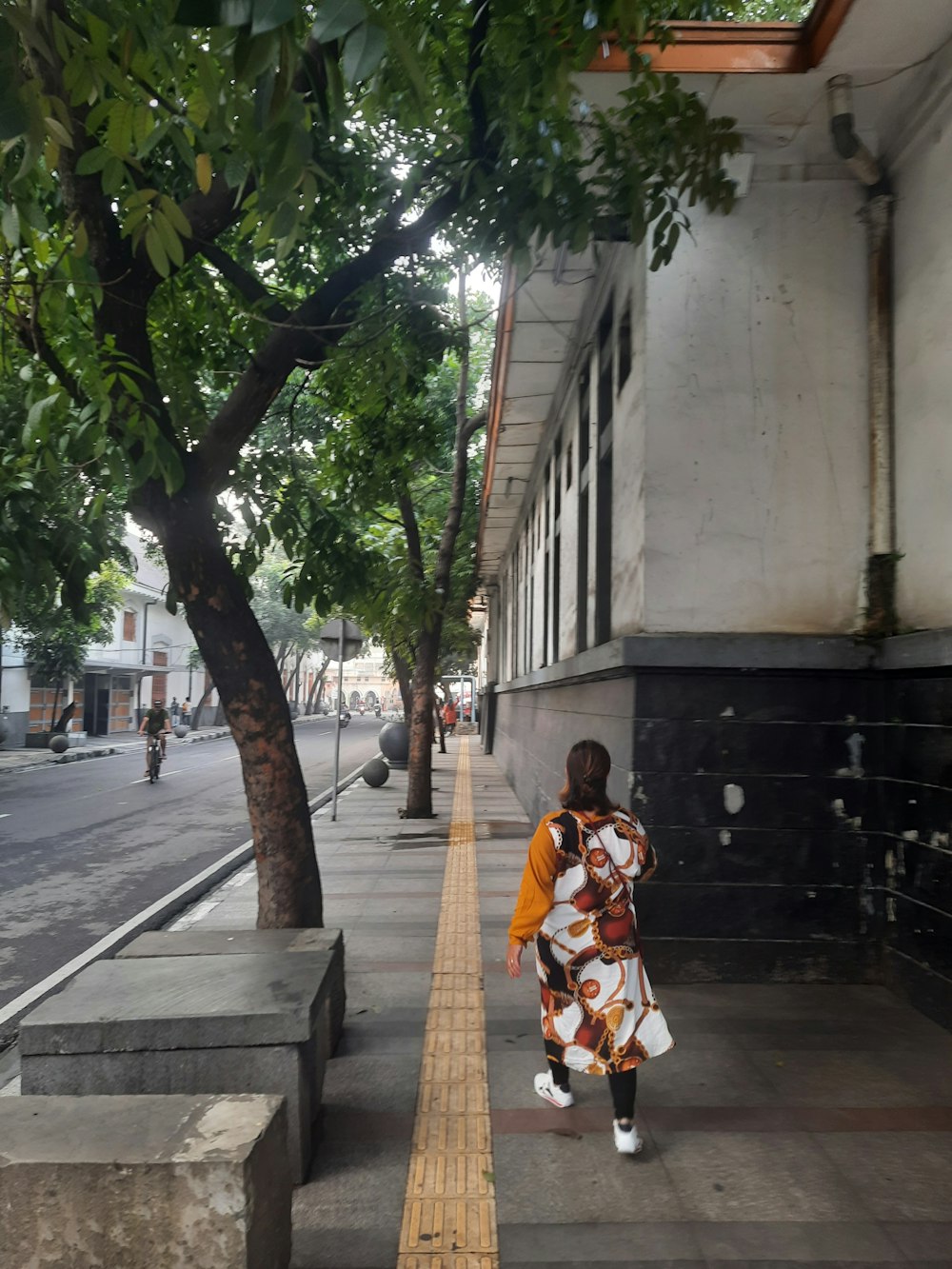 Eine Frau geht einen Bürgersteig neben einem Baum entlang