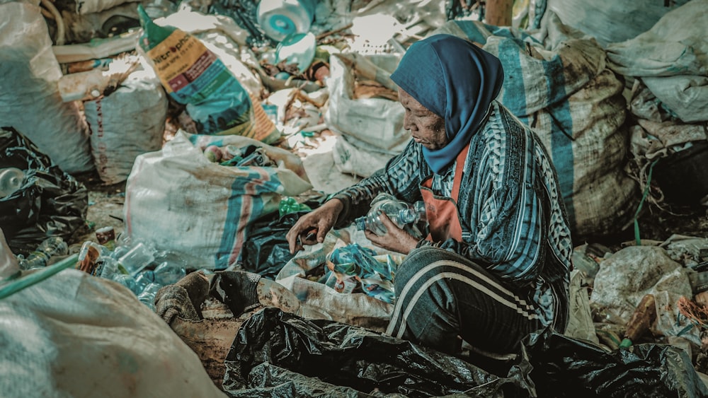 a woman sitting on the ground surrounded by bags of garbage