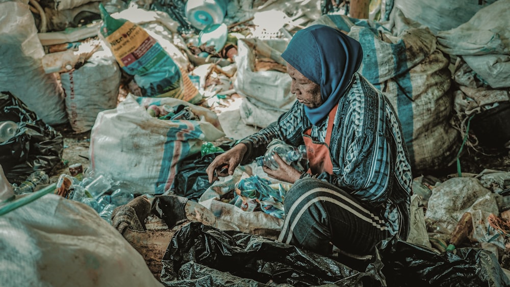 une femme assise par terre entourée de sacs d’ordures