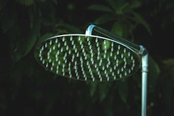 a close up of a shower head in front of trees
