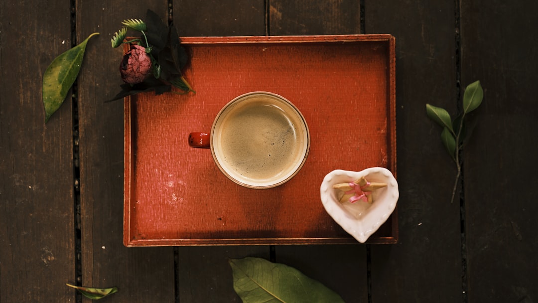 a cup of coffee with a heart shaped napkin on a tray, a hot fresh coffee on a red wooden tray
