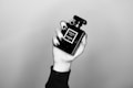 A hand with black nail polish is holding a black perfume bottle labeled 'Coco Noir Chanel Paris.' The image is in black and white, showcasing a minimalist and elegant aesthetic.