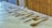 A collection of various silver kitchen utensils is neatly arranged on a white marble countertop. The assortment includes tongs, spatulas, and forks, each displayed in an orderly fashion. The background shows wooden cabinetry, adding warmth to the image.