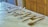 A collection of various silver kitchen utensils is neatly arranged on a white marble countertop. The assortment includes tongs, spatulas, and forks, each displayed in an orderly fashion. The background shows wooden cabinetry, adding warmth to the image.