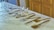 A collection of various silver kitchen utensils is neatly arranged on a white marble countertop. The assortment includes tongs, spatulas, and forks, each displayed in an orderly fashion. The background shows wooden cabinetry, adding warmth to the image.