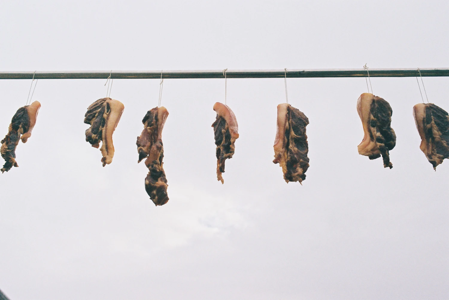 Strips of marinated meat hanging from a line to dry in the air