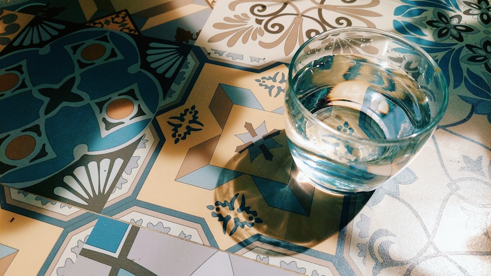 a glass of water sitting on top of a tiled floor